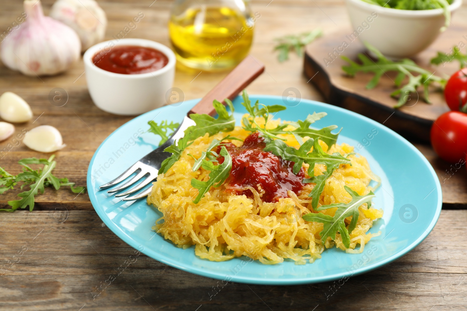 Photo of Tasty spaghetti squash with tomato sauce and arugula served on wooden table