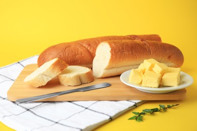 Photo of Whole and cut baguettes with fresh butter on yellow background