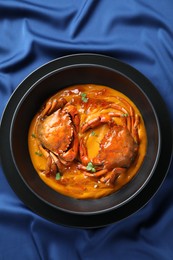 Delicious boiled crabs with sauce in bowl on blue tablecloth, top view