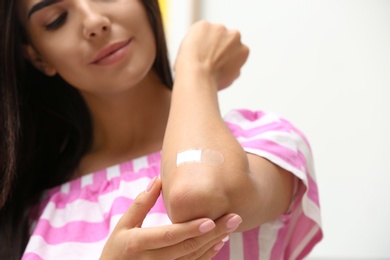Photo of Woman with adhesive bandage on elbow against light background, closeup