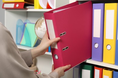 Photo of Woman taking binder office folder from shelving unit, closeup