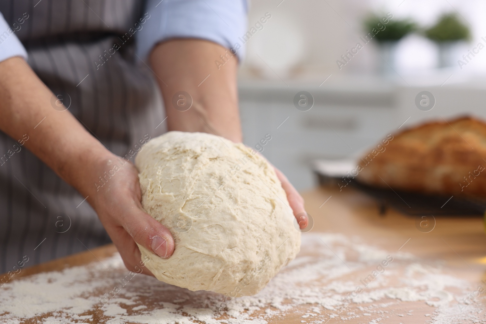 Photo of Making bread. Man kneading dough at wooden table in kitchen, closeup