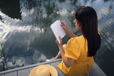 Woman reading book on pier near lake, above view