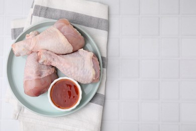 Photo of Fresh marinade and raw chicken drumsticks on white tiled table, top view. Space for text