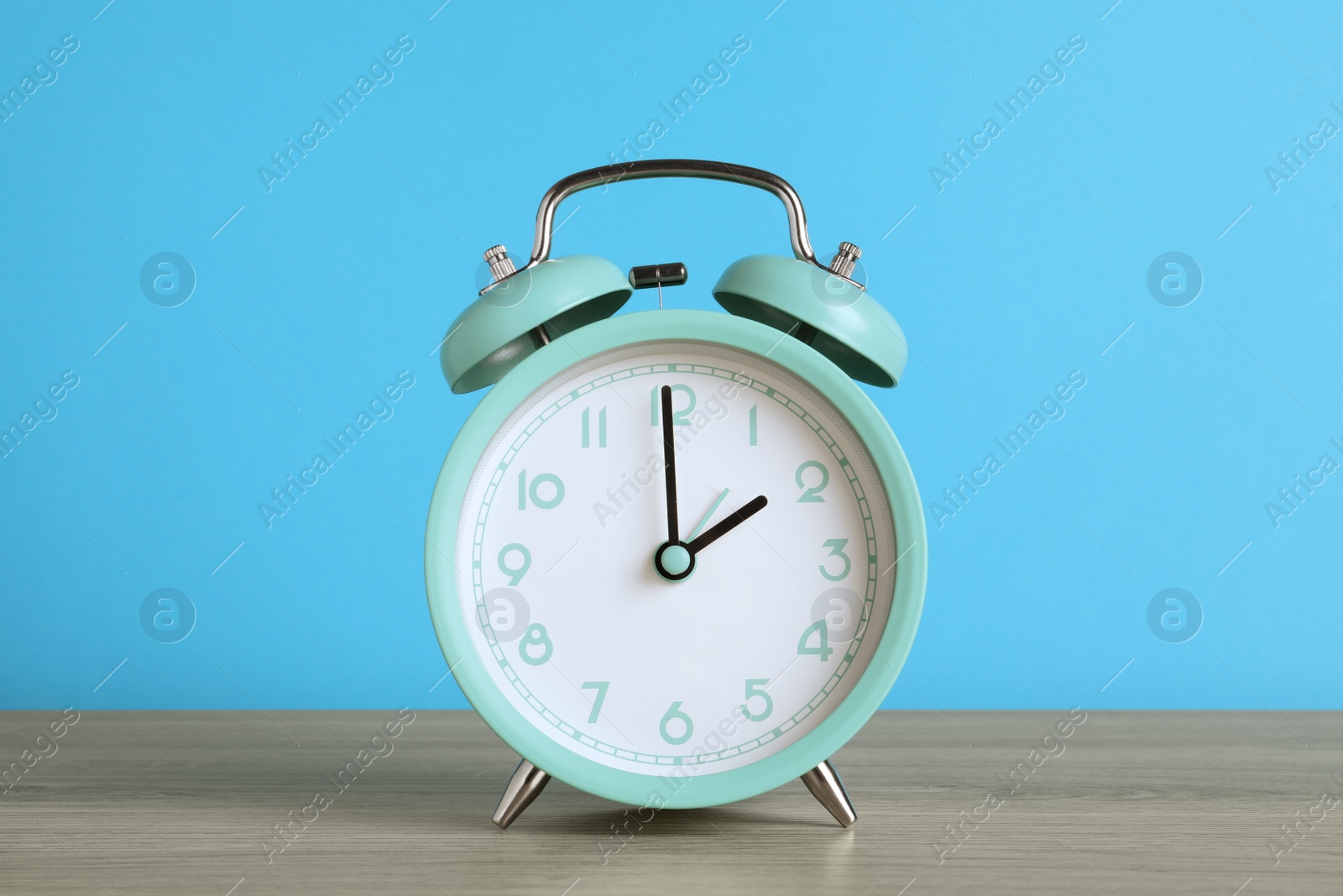 Photo of Turquoise alarm clock on wooden table against light blue background