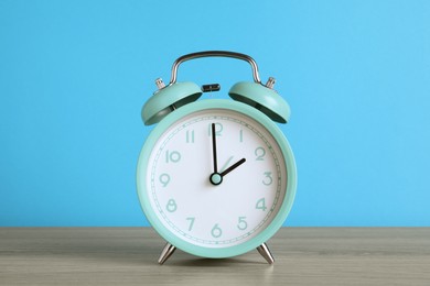 Photo of Turquoise alarm clock on wooden table against light blue background