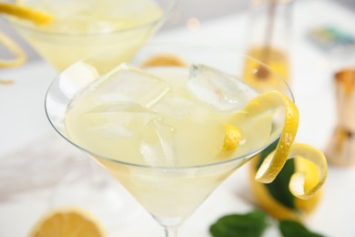 Photo of Delicious bee's knees cocktail with ice and lemon twist on white table, closeup