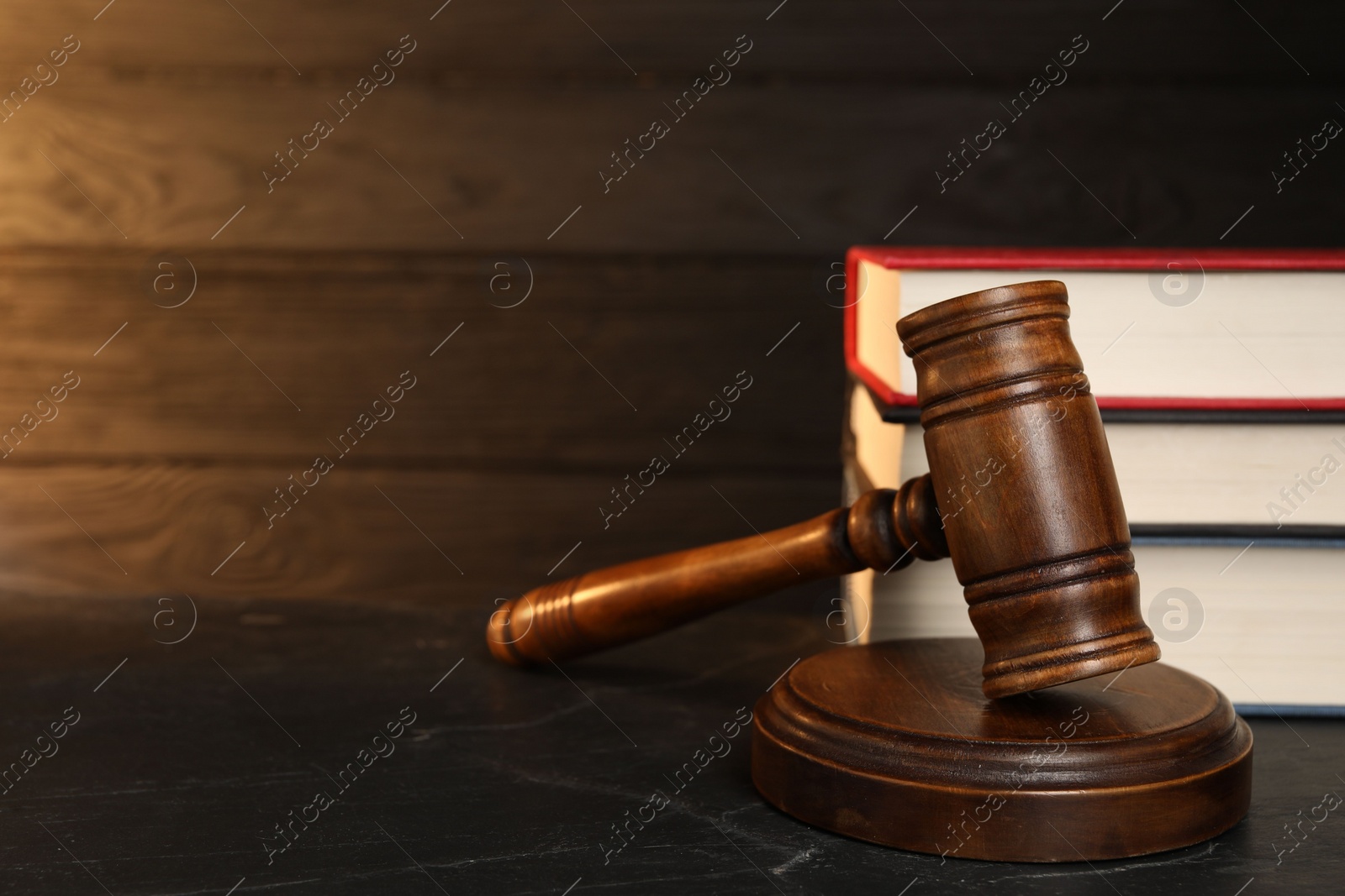 Photo of Wooden gavel and stack of books on dark textured table, closeup. Space for text