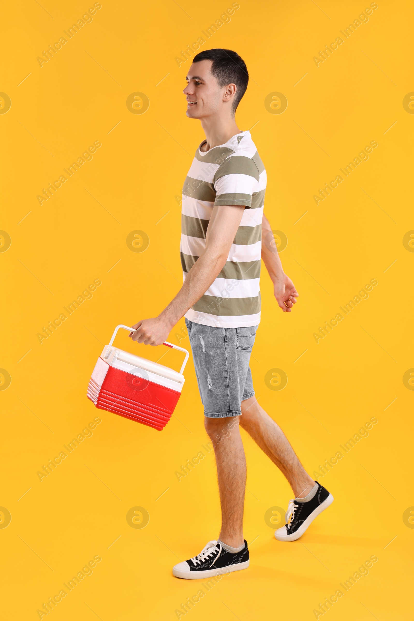 Photo of Man with red cool box walking on orange background