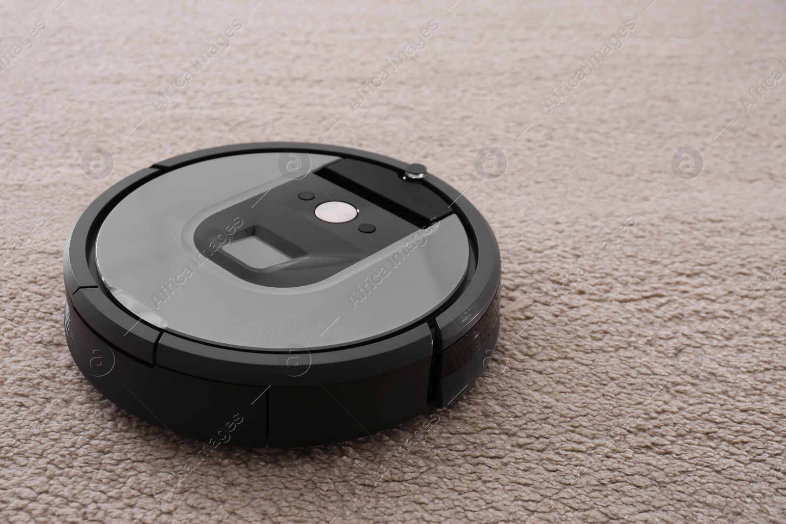 Photo of Modern robotic vacuum cleaner on beige carpet