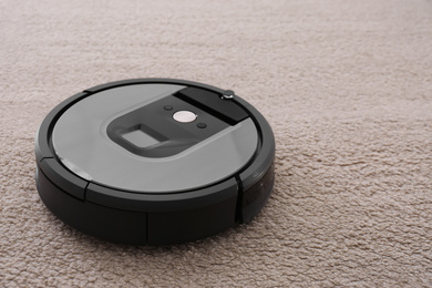 Modern robotic vacuum cleaner on beige carpet