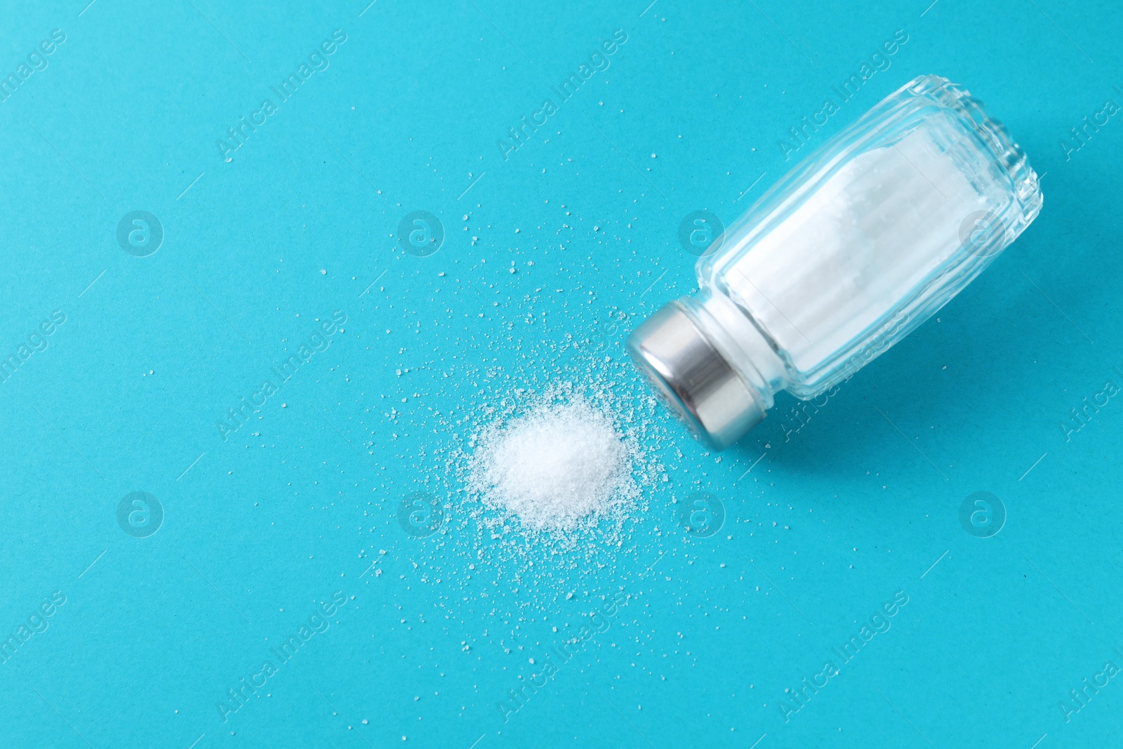 Photo of Organic white salt in glass shaker on light blue background, top view. Space for text