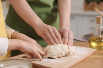 Photo of Making bread. Mother and her daughter kneading dough at wooden table in kitchen, closeup