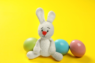 Cute Easter bunny toy and dyed eggs on color background