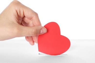 Photo of Woman putting red heart into slot of donation box against white background, closeup