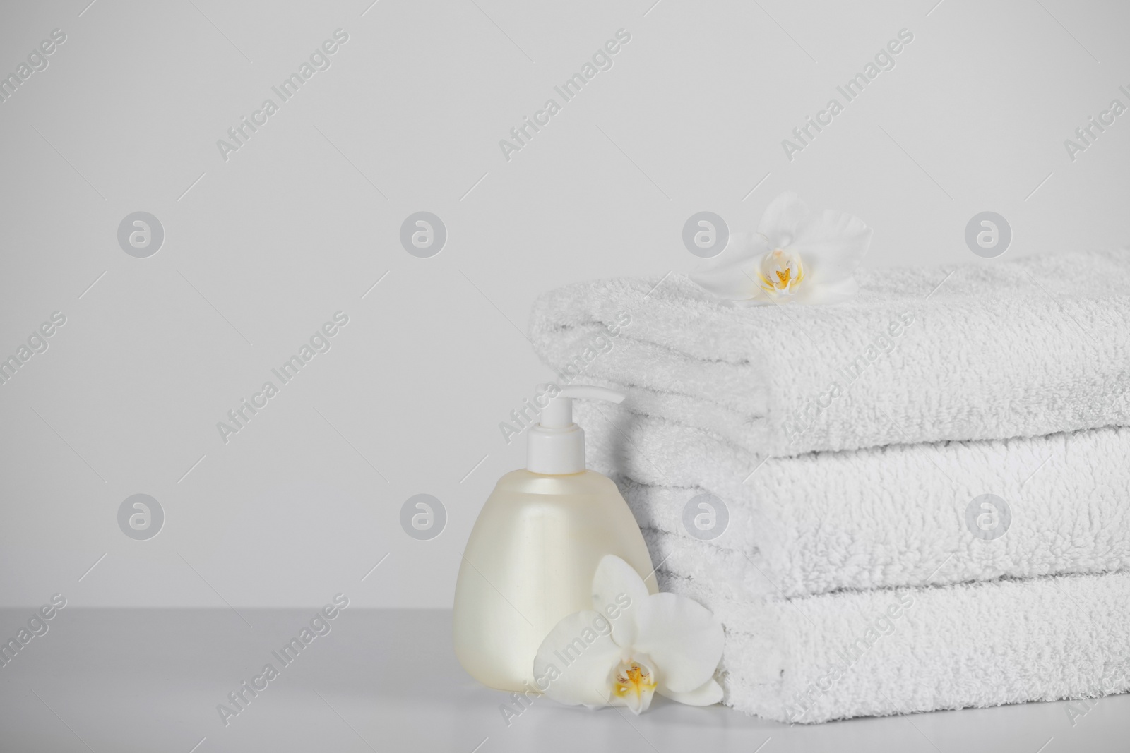 Photo of Soft folded towels, orchid flowers and dispenser on white table, space for text