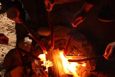 People roasting sausages on campfire outdoors at night, closeup