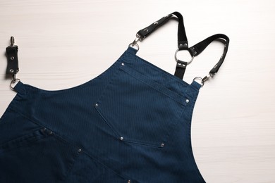 Photo of Stylish dark blue apron on white wooden table, top view. Mockup for design