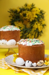 Traditional Easter cakes with sprinkles, painted eggs and beautiful spring flowers on yellow background