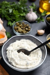 Tasty tartar sauce and ingredients on black table