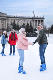 Image of Happy couple with friends skating along ice rink outdoors