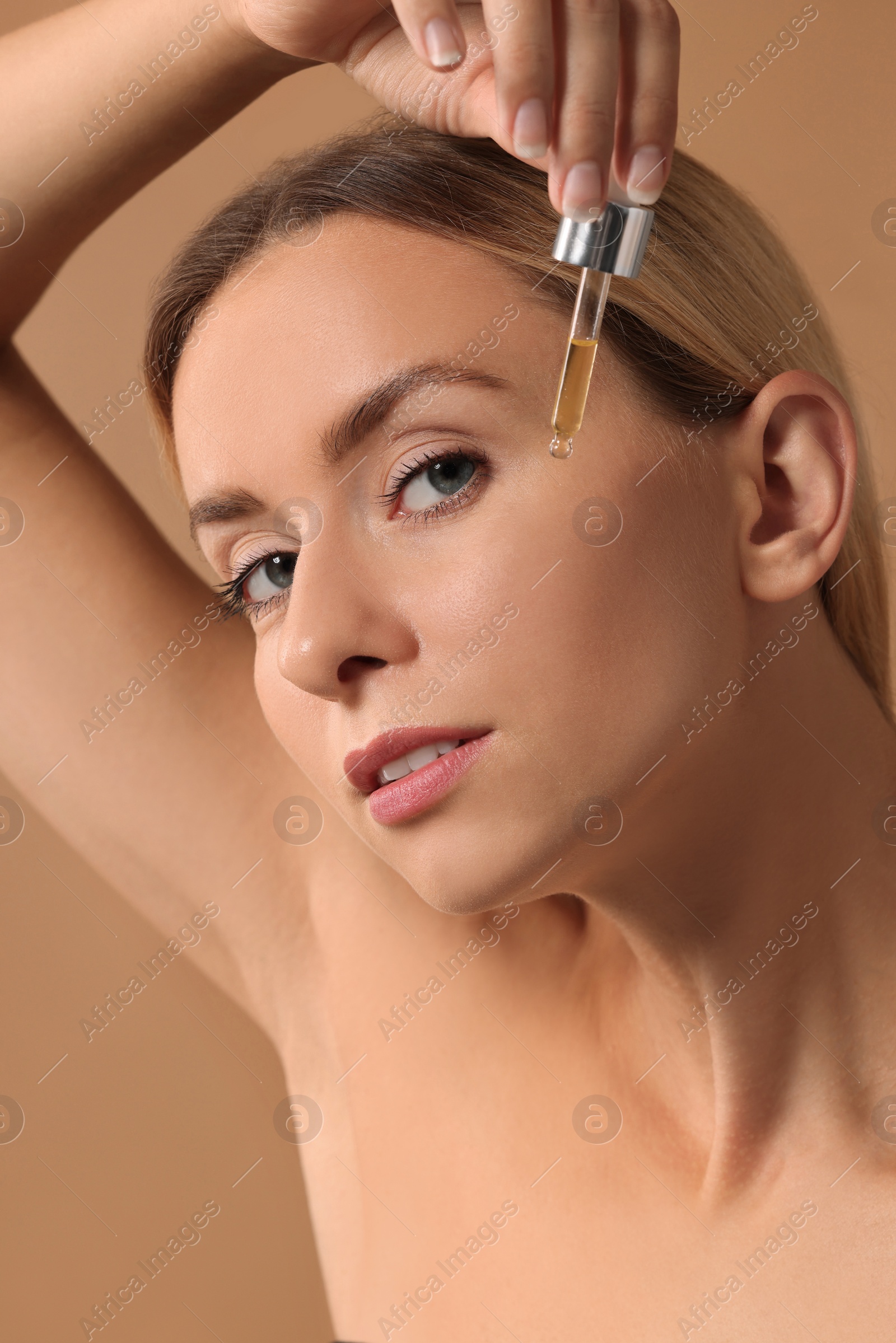 Photo of Beautiful woman applying cosmetic serum onto her face on beige background