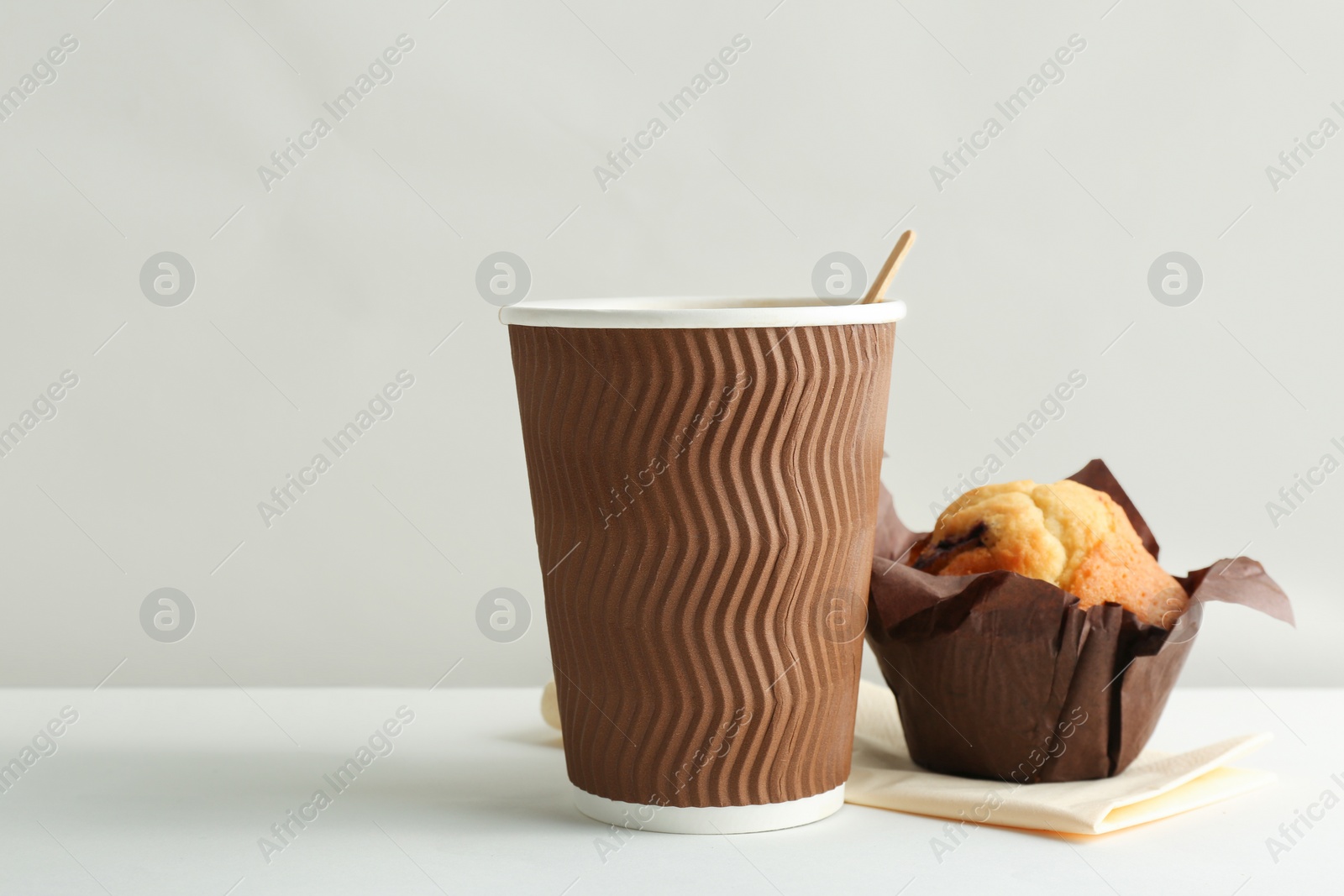 Photo of Hot aromatic coffee in paper cup and tasty muffin on white background
