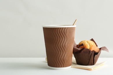 Hot aromatic coffee in paper cup and tasty muffin on white background