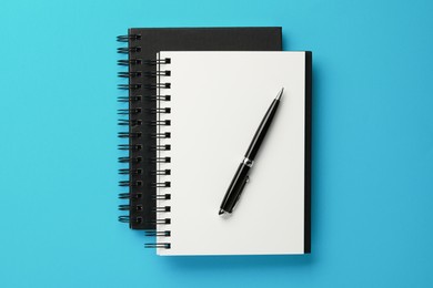 Photo of Notebooks and pen on light blue background, top view