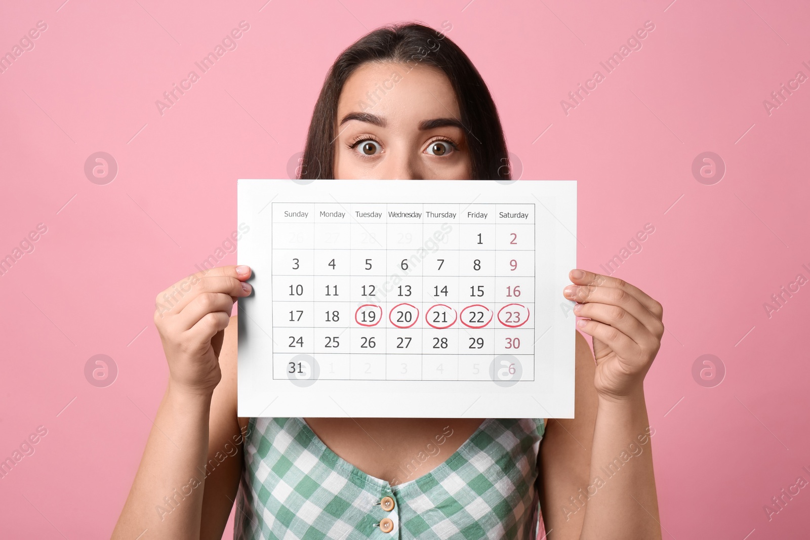 Photo of Young woman holding calendar with marked menstrual cycle days on pink background