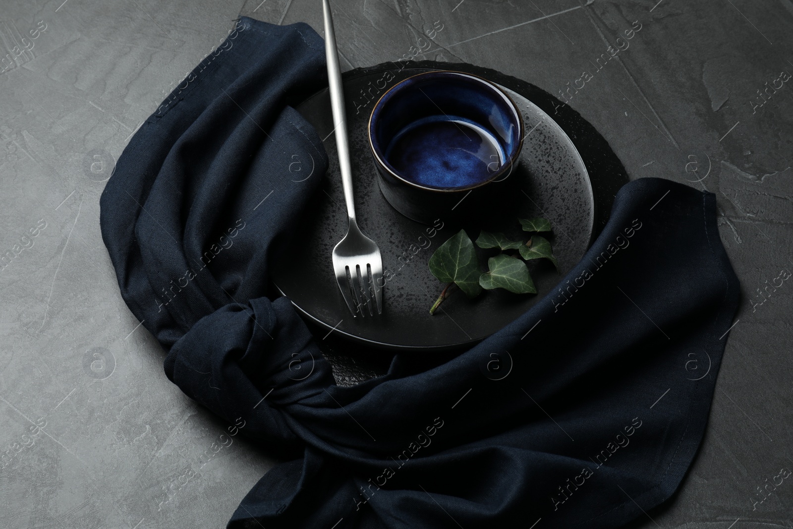 Photo of Stylish table setting. Dishes, fork, napkin and green leaves on grey surface