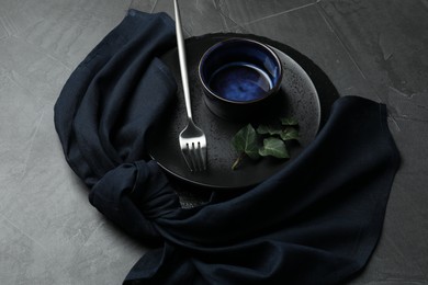 Photo of Stylish table setting. Dishes, fork, napkin and green leaves on grey surface