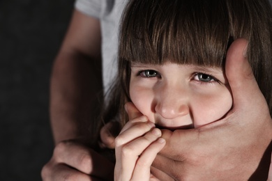 Photo of Adult man covering scared little girl's mouth, closeup with space for text. Child in danger