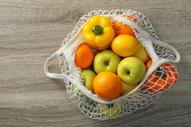 Net bag with vegetables and fruits on wooden table, top view