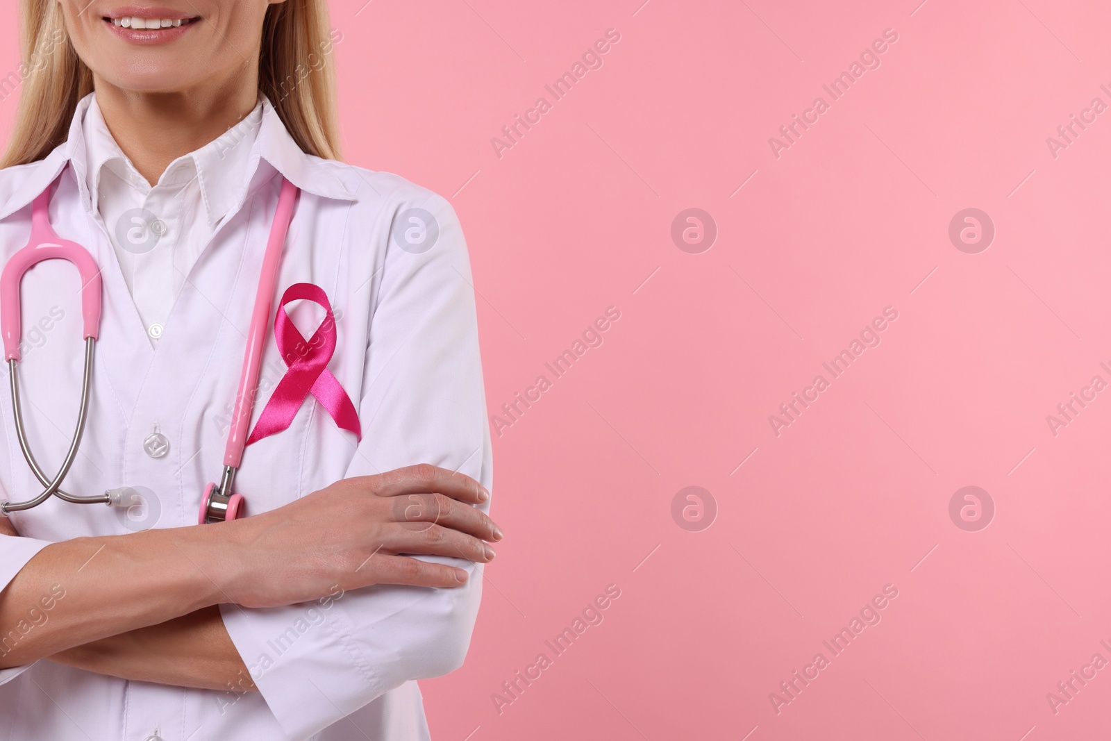 Photo of Doctor with pink ribbon and stethoscope on color background, closeup and space for text. Breast cancer awareness