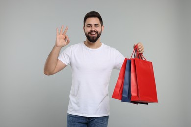 Photo of Happy man with many paper shopping bags showing ok gesture on grey background