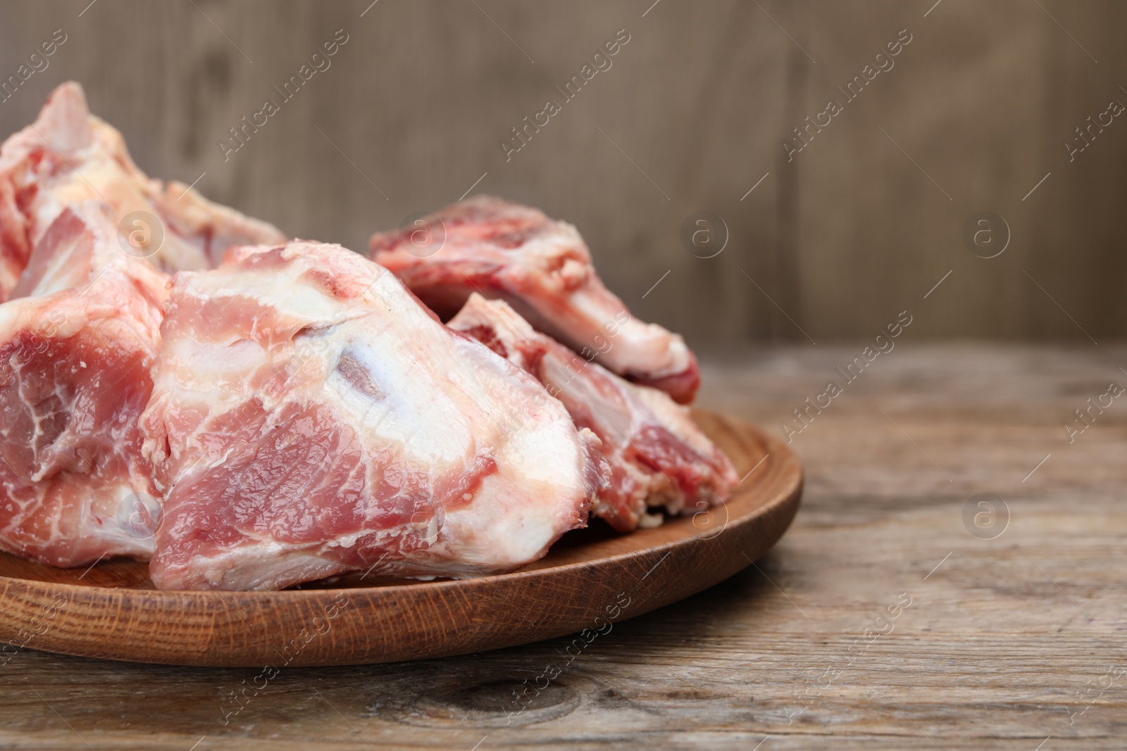 Photo of Plate with raw chopped meaty bones on wooden table, closeup. Space for text