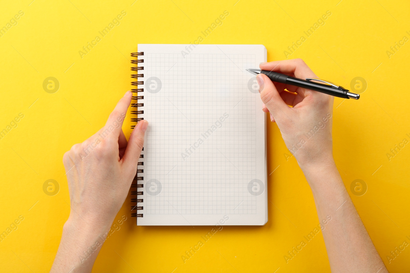 Photo of Woman writing in notebook on yellow background, top view