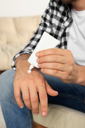 Photo of Man applying cream from tube onto hand indoors, closeup