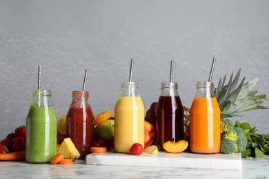 Bottles of delicious juices and fresh fruits on white marble table