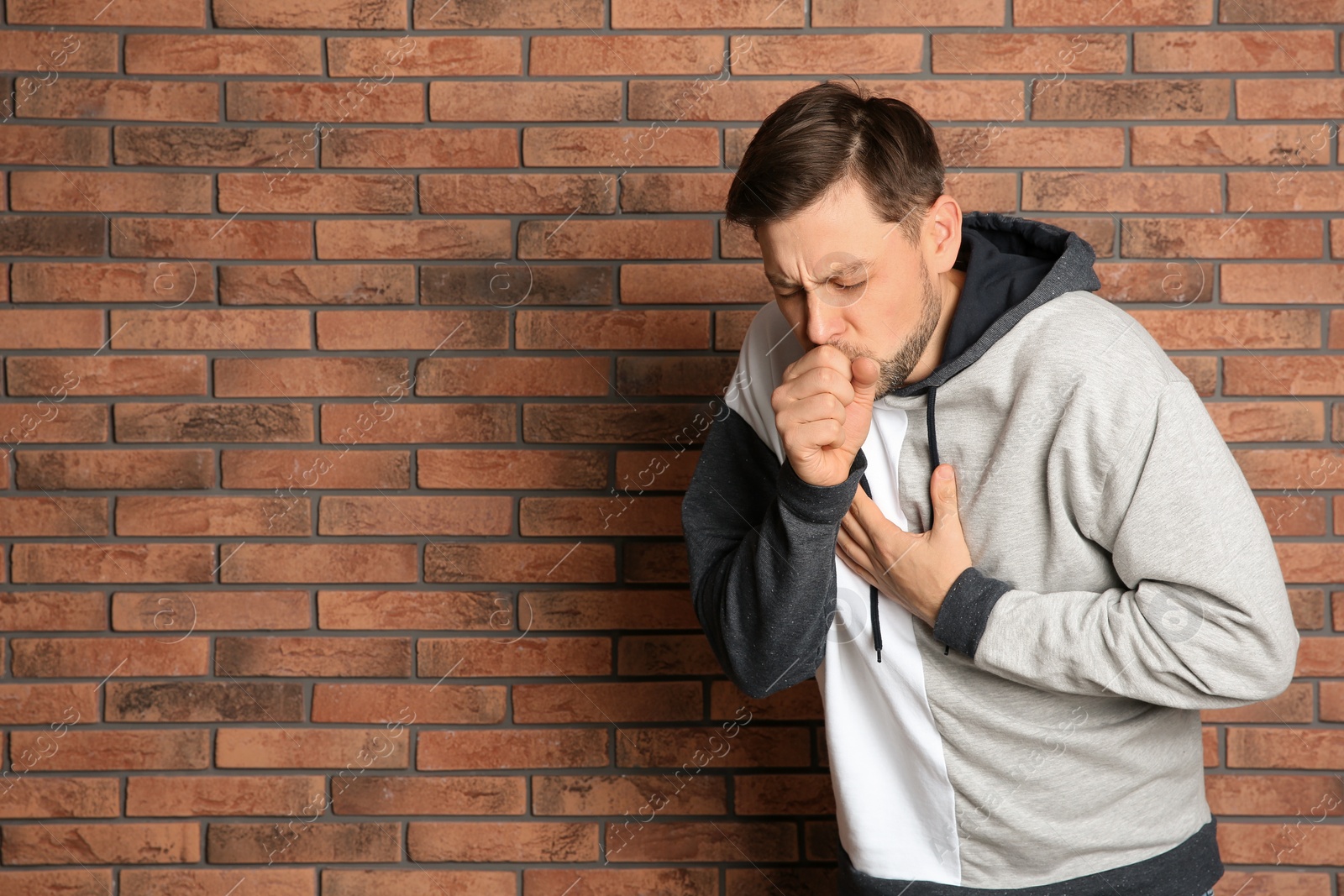 Photo of Man suffering from cough near brick wall. Space for text