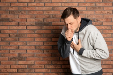 Man suffering from cough near brick wall. Space for text