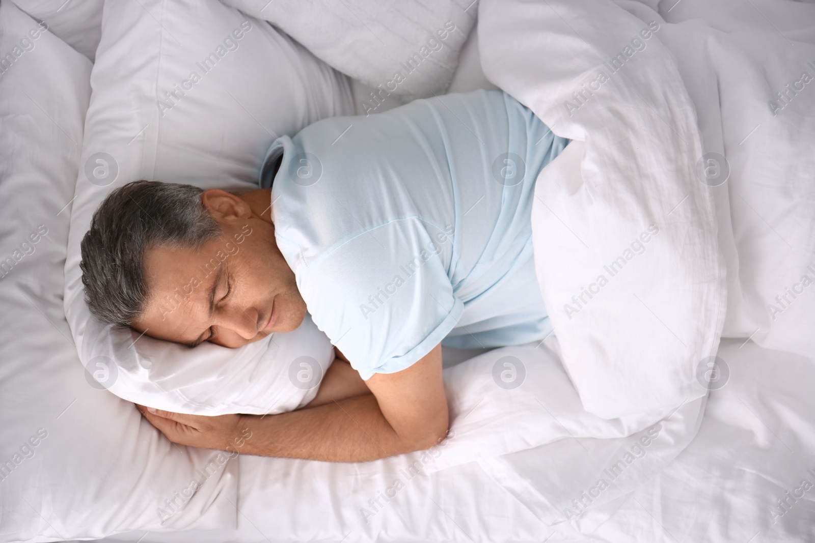 Photo of Man sleeping on comfortable pillow in bed at home, top view