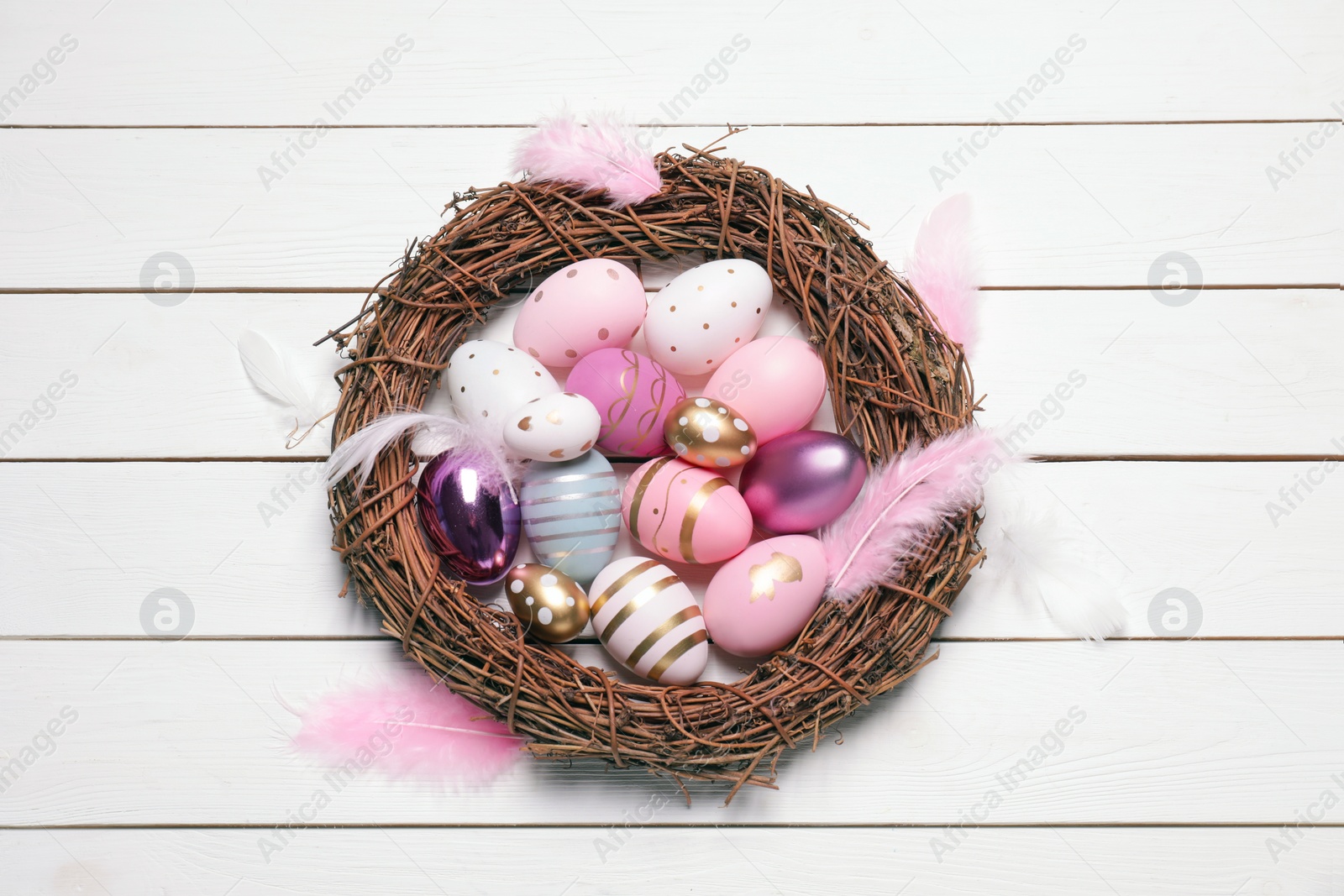 Photo of Festively decorated Easter eggs, vine wreath and feathers on white wooden table, top view