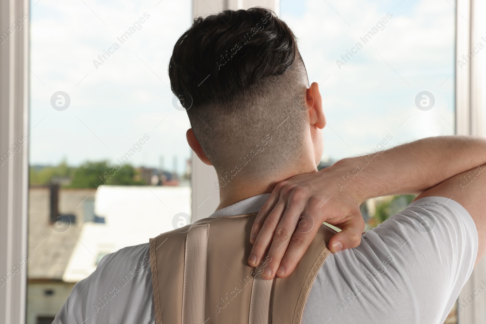 Photo of Man with orthopedic corset near window indoors, back view