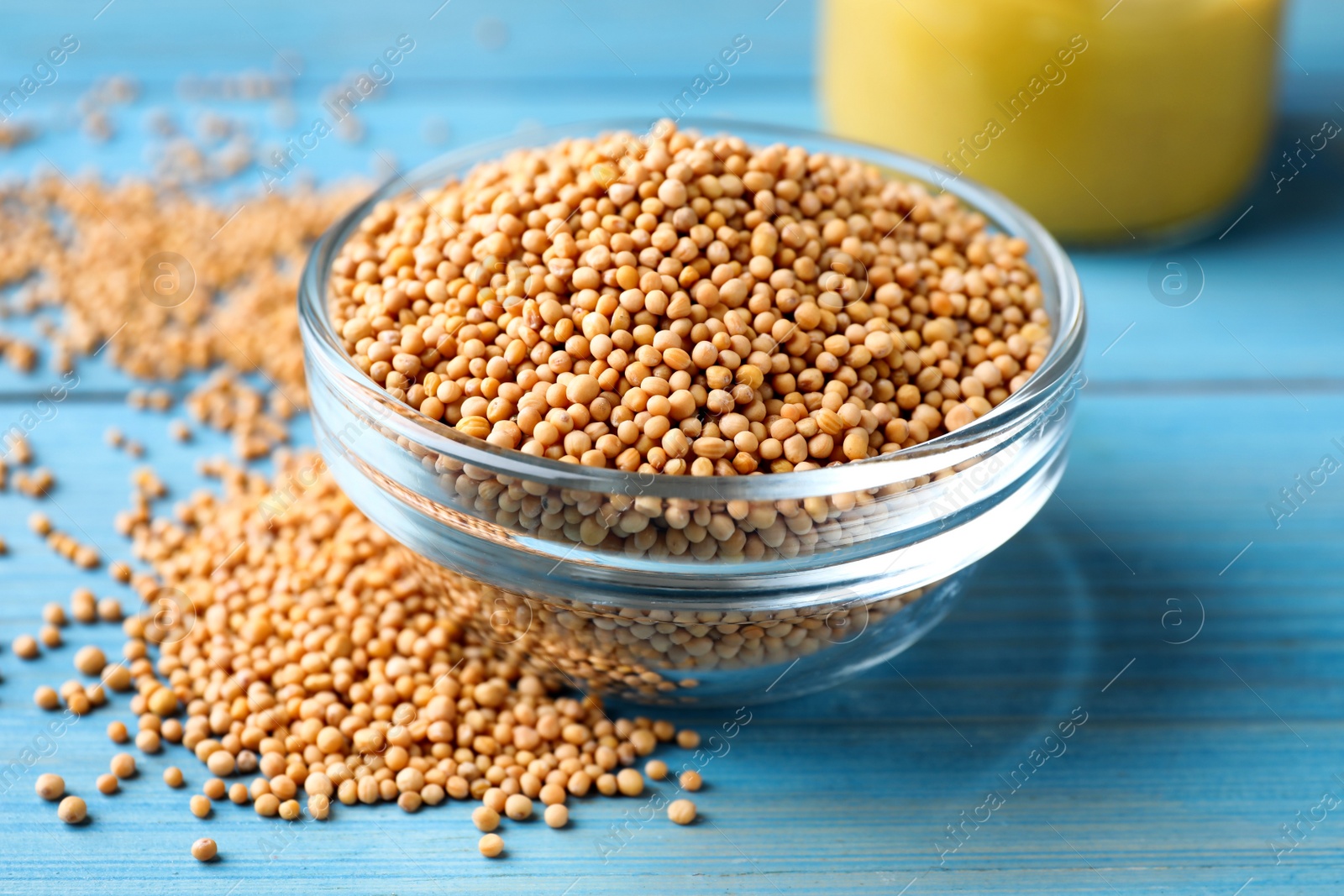 Photo of Mustard seeds in glass bowl on turquoise wooden table, closeup