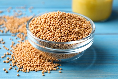 Photo of Mustard seeds in glass bowl on turquoise wooden table, closeup