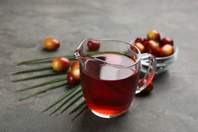 Photo of Palm oil in glass jug, tropical leaf and fruits on grey table