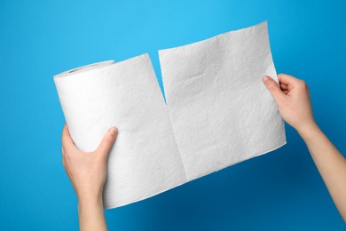 Woman tearing paper towels on light blue background, closeup