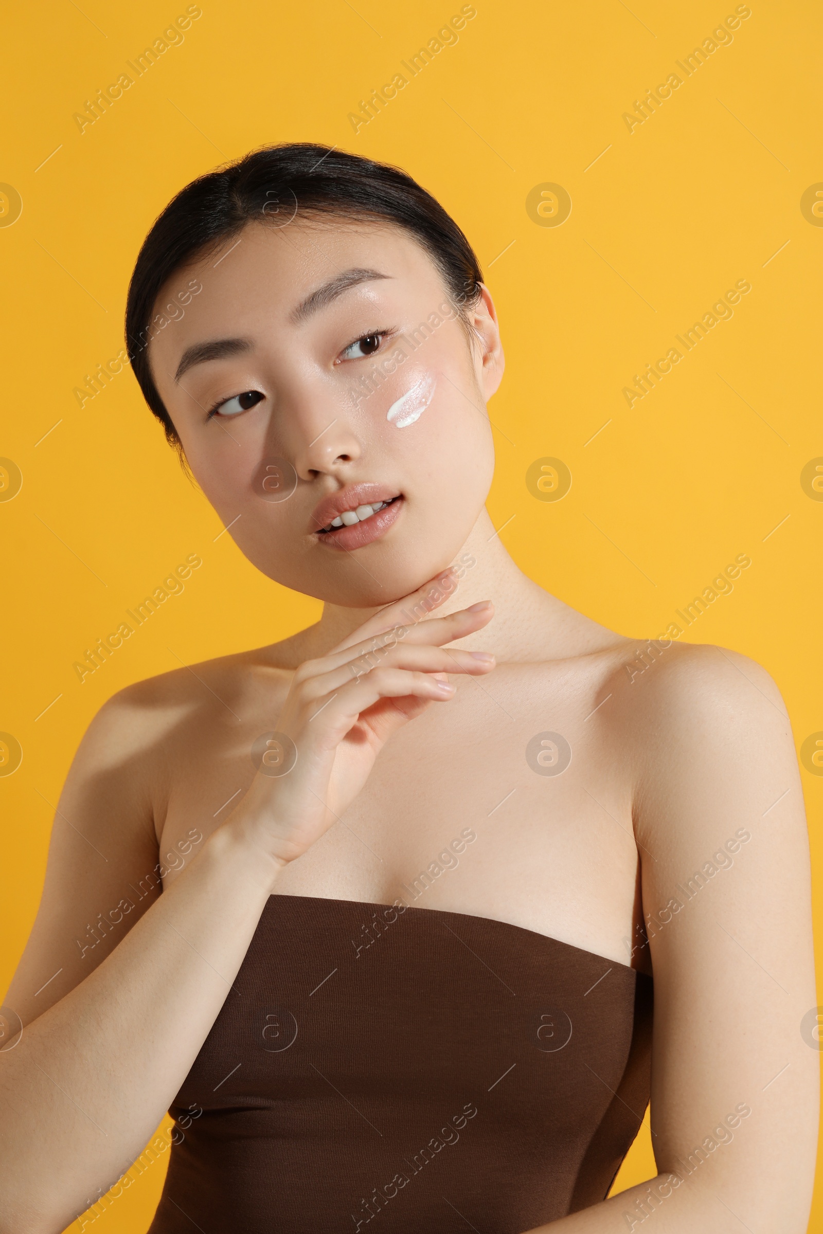 Photo of Beautiful young woman with sun protection cream on her face against orange background